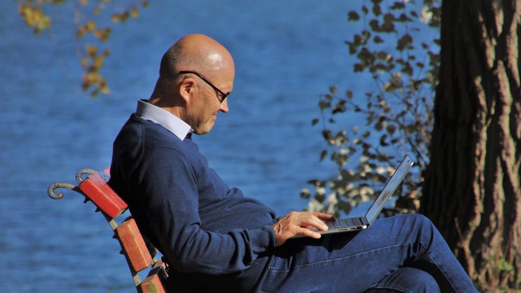 海辺のベンチでノートパソコンを操作する年配の男性