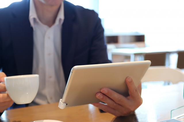 コーヒーを飲みながらタブレットを見る男性