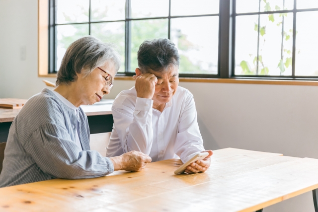 スマホを見ながら頭を抱える高齢者夫婦