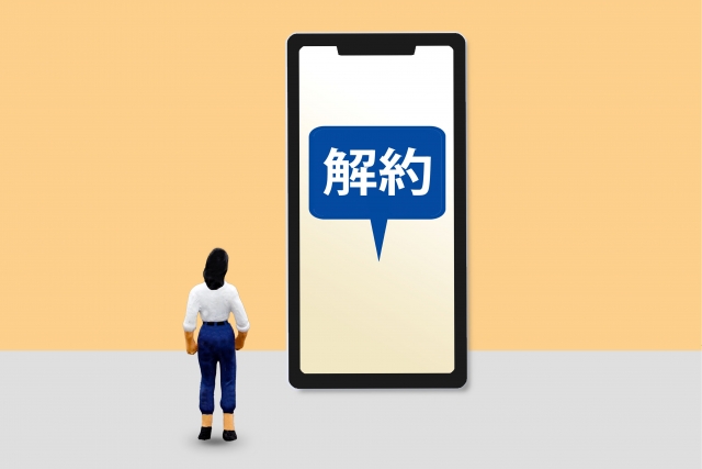 画面に「解約」とあるスマホを見つめる人形