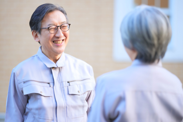 向かい合って話す作業着の男性と女性の後ろ姿