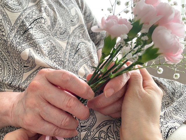 花を持つ高齢女性の手を握る女性の手元