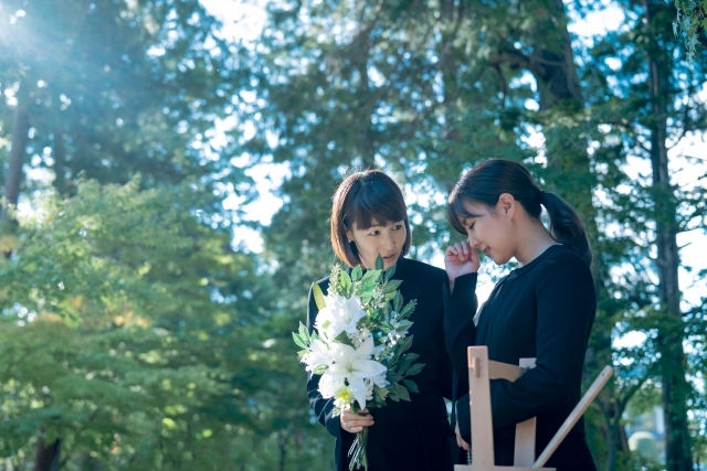 喪服姿で泣く女性とユリを抱えながらなぐさめる女性