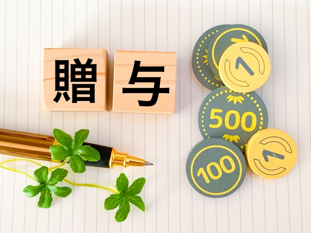 贈与と書かれた木のブロックとボールペンとオモチャのコイン