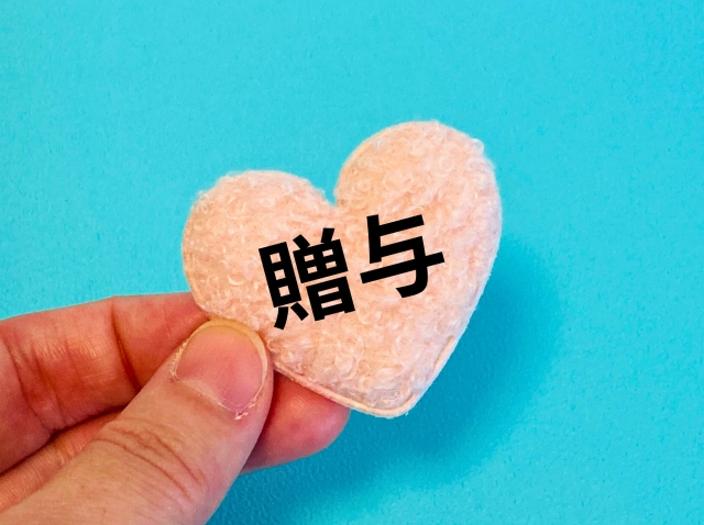 贈与と書かれたピンクのハートを持つ手元
