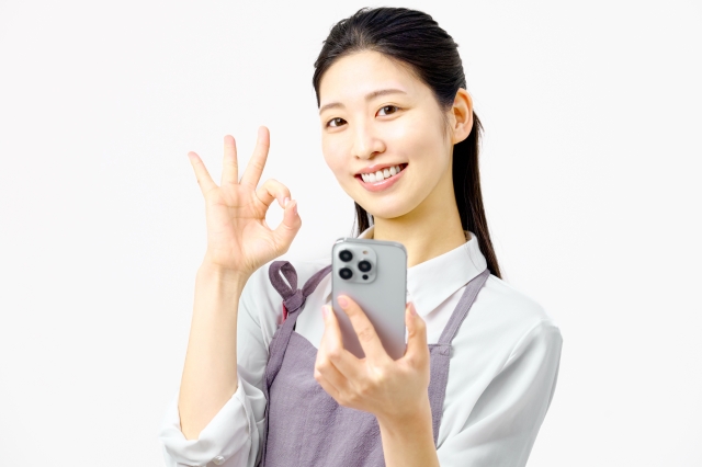 スマホを見ながら指でOKマークを作る主婦
