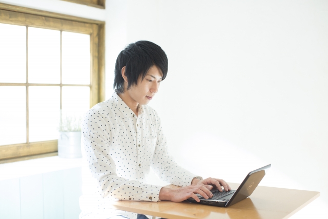 白い部屋でノートパソコンを広げる男性